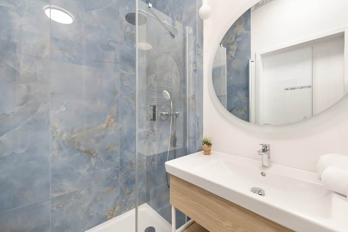 Un baño con cabina de ducha de vidrio, un espejo redondo, un lavabo blanco y un mueble de tocador de madera.