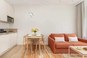 A modern living space with a dining area, a sofa, and a kitchen area.