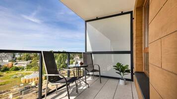 Ein Balkon mit zwei Stühlen, einem Tisch, einer Topfpflanze und Blick auf die Stadt.