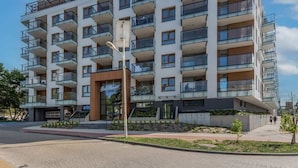 A multi-story residential building with balconies, a central entrance, and a paved area with small trees. - Modern Apartment with Balcony | Parking, 450 m to the Beach (Miedzyzdroje)