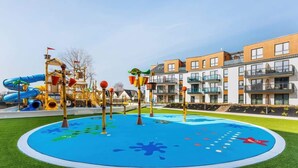 A playground with slides and climbing structures, surrounded by modern residential buildings. - Modern Apartment with Balcony | Parking, 450 m to the Beach (Miedzyzdroje)