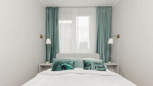 Un dormitorio ordenado con una cama, dos mesitas de noche y un ventanal con cortinas.