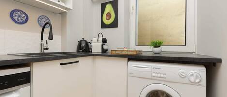 Cocina compacta con lavavajillas integrado, lavadora y ventana con vistas.
