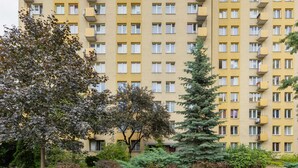 Un edificio residencial de varios pisos con balcones, rodeado de árboles y arbustos.