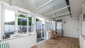 A covered patio with a view of the sea, a washing machine, and a chair. - Tan Y Wylan -  a bungalow that sleeps 6 guests  in 3 bedrooms (Rhosneigr)
