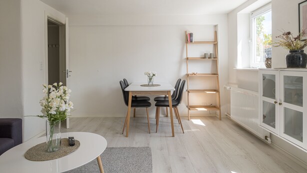 Uma sala de estar moderna com uma mesa de jantar, cadeiras, uma estante e um radiador.