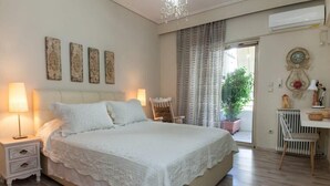 A bedroom with a large bed, bedside lamps, a chair, a desk, and a potted plant.