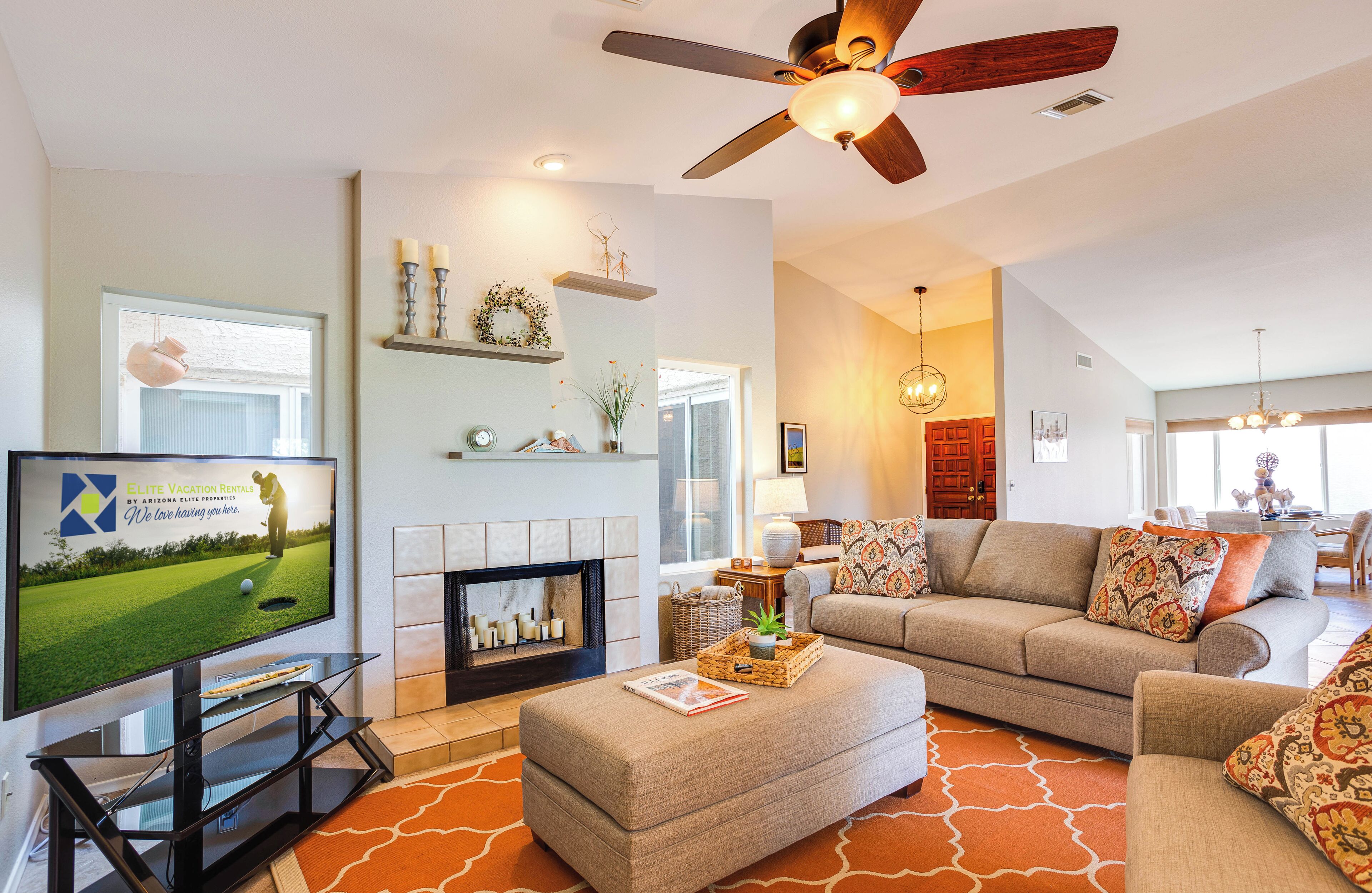 A modern living room with a flat-screen TV, a fireplace, a ceiling fan, and a sofa.