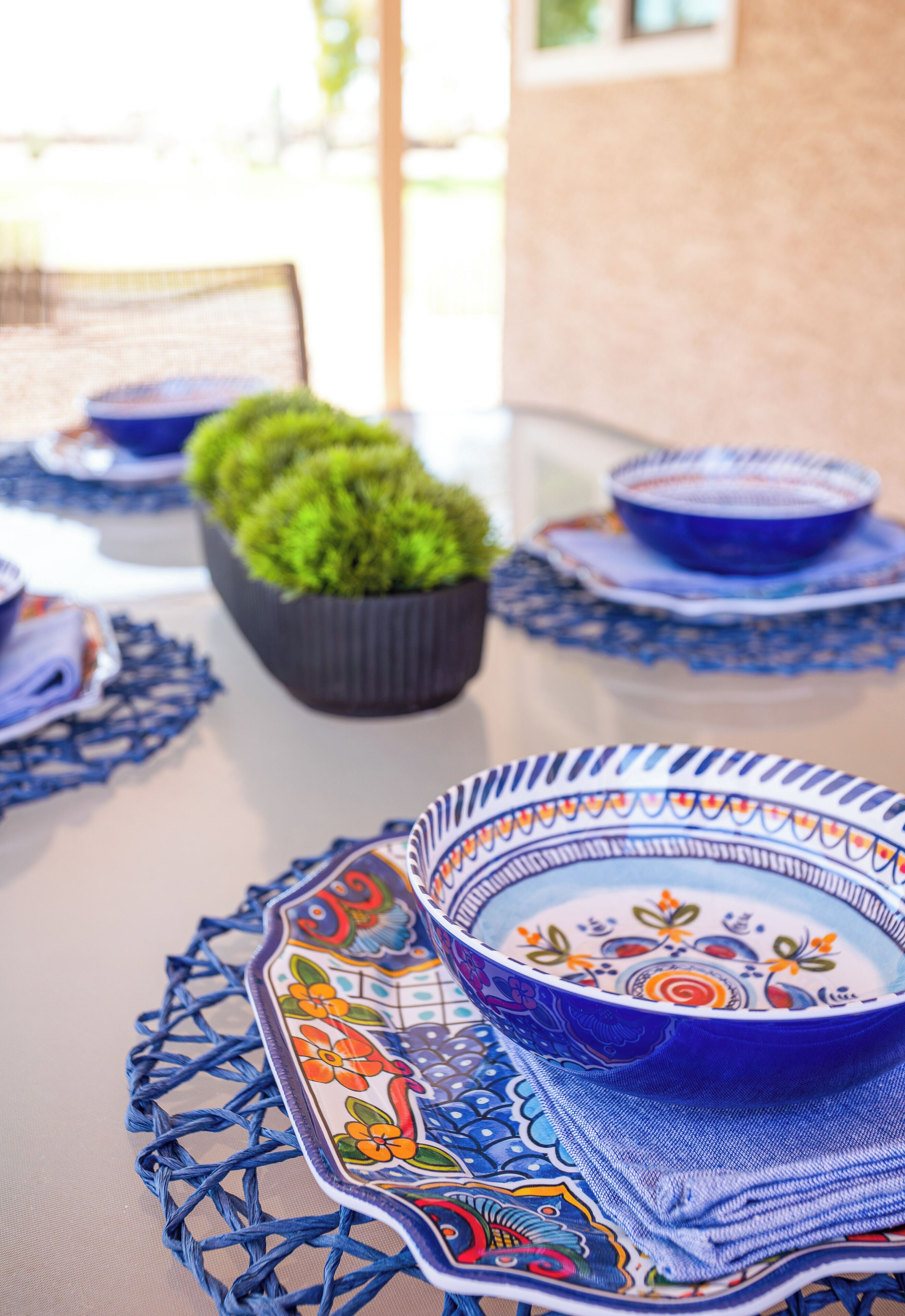 A table set with blue and white patterned tableware, a potted plant, and a blue chair.