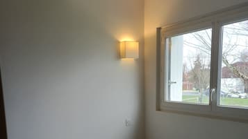 Simple, cozy space with a bed, stool, and window offering a view.