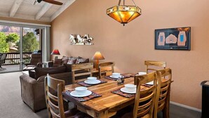 Un comedor con una mesa de madera dispuesta para cuatro personas, rodeada de sillas de madera, un ventilador de techo y una lámpara decorativa.