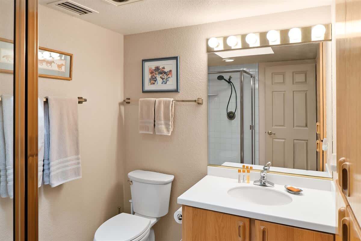 A bathroom with a toilet, sink, mirror, and shower.