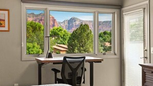 Una habitación con escritorio, silla y ventana con vistas a montañas y árboles.