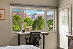 Una habitación con escritorio, silla y ventana con vistas a montañas y árboles.