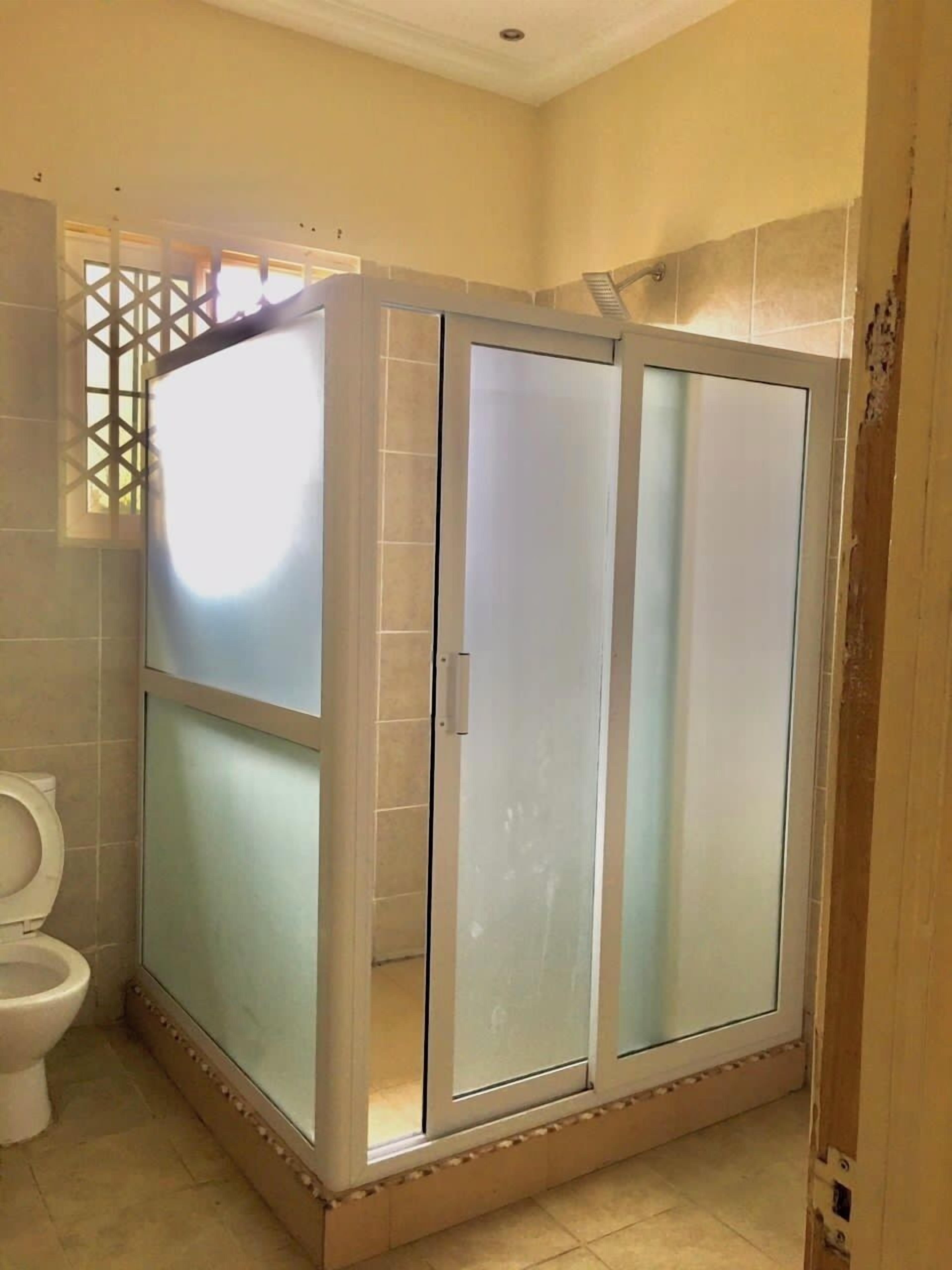 Un baño con cabina de ducha de vidrio, inodoro y ventana con celosía decorativa.