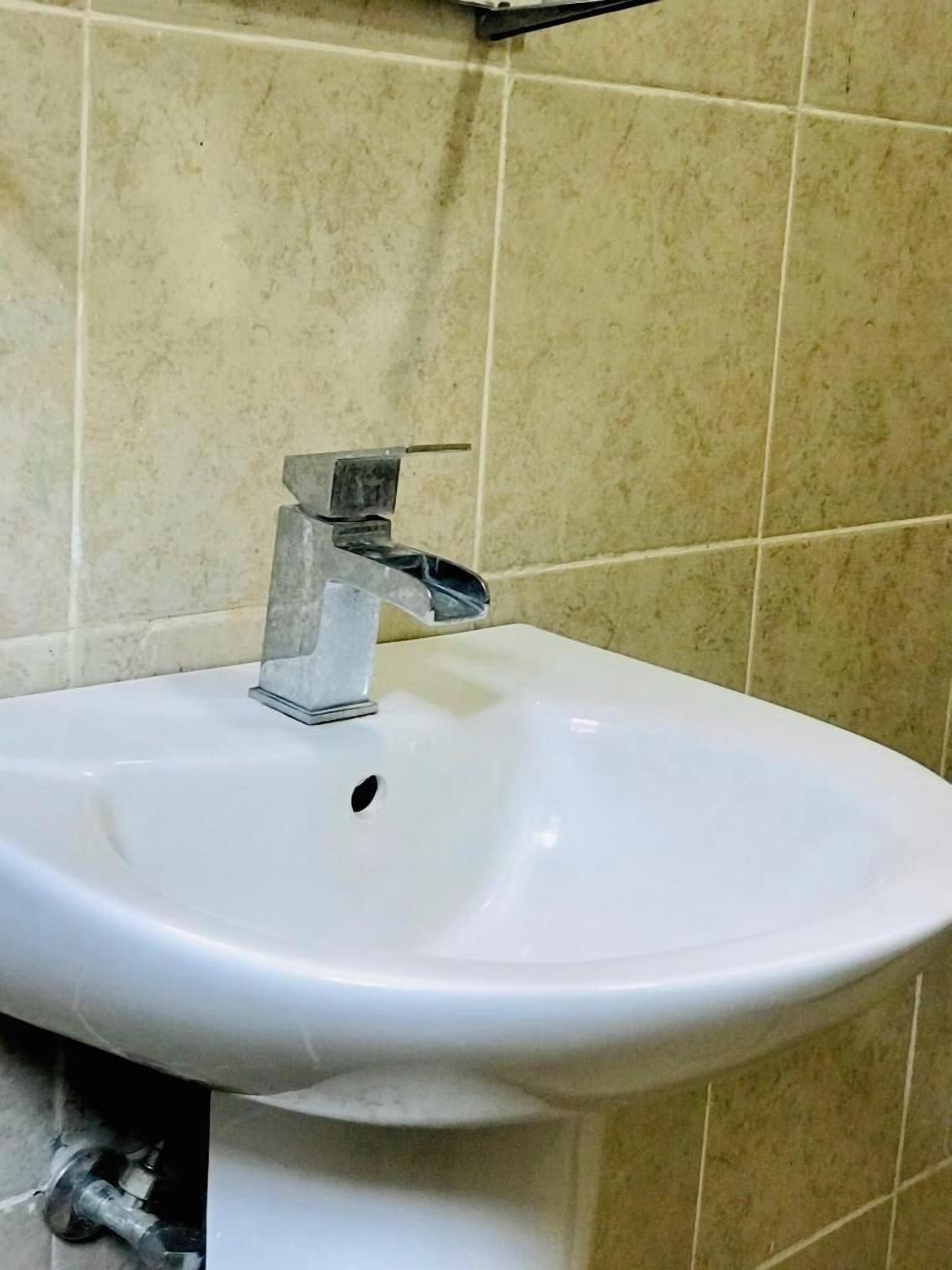 A white bathroom sink with a chrome faucet, set against beige tiled walls.
