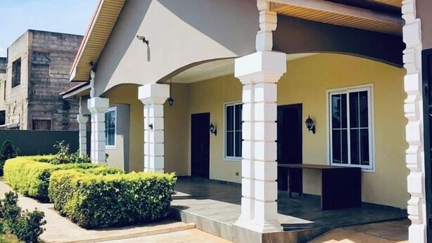 A modern building with a covered entrance, white columns, and a tiled patio area. - Cosy family villa providing a relaxing atmosphere in Tema .Close to restaurants. (Tema)