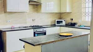 A modern kitchen with white cabinets, a central island, a microwave, and a stove. - Cosy family villa providing a relaxing atmosphere in Tema .Close to restaurants. (Tema)