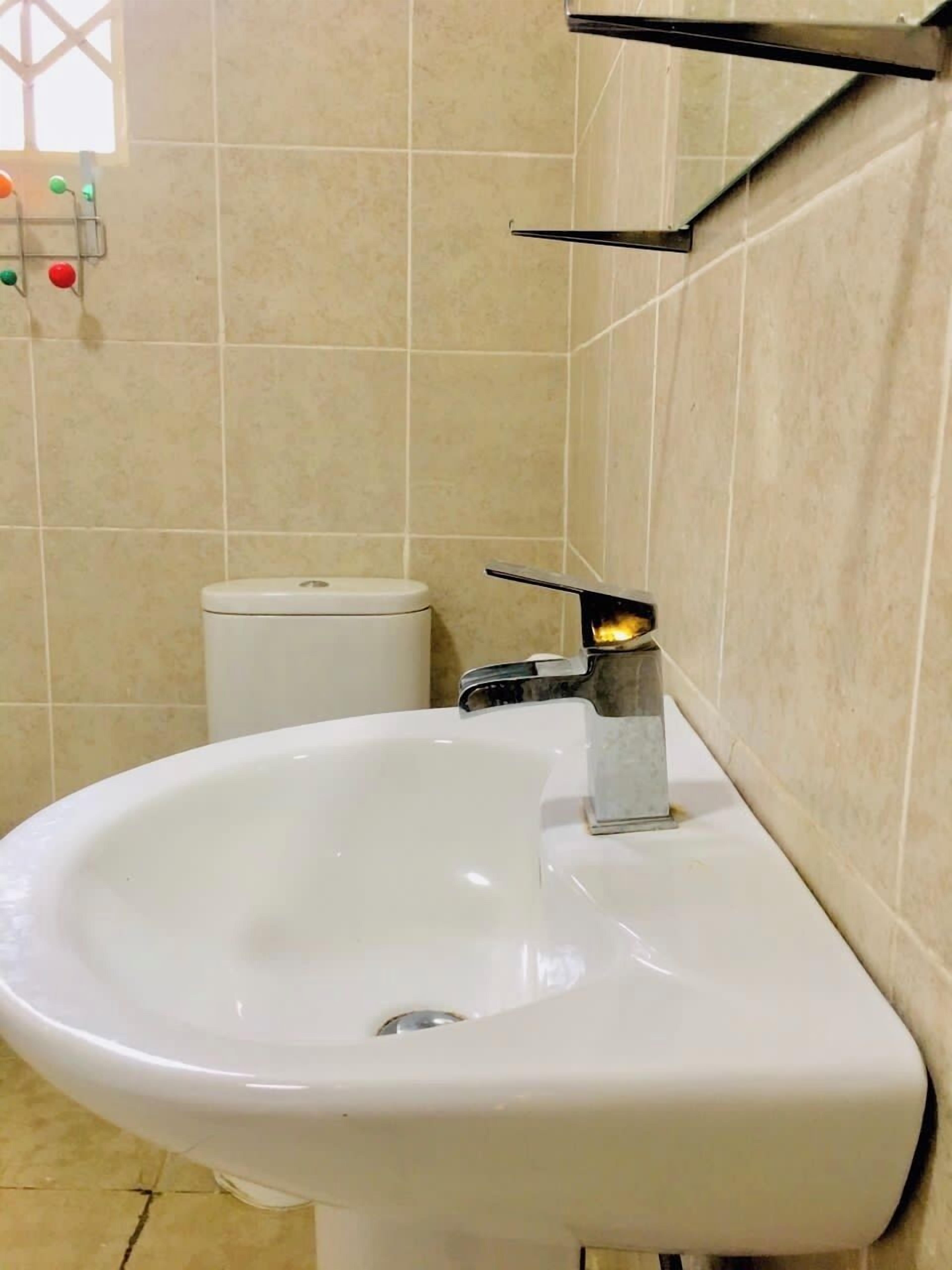 A bathroom with a white sink, a toilet, and a wall-mounted shelf.