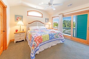 Quarto com cama, duas mesas de cabeceira, ventoinha no teto, janela com vista e porta.