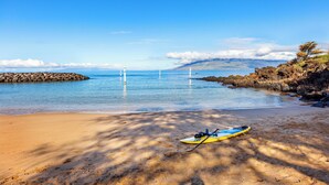 A beach with a kayak on the sand, a rocky shoreline, and a clear blue sky.