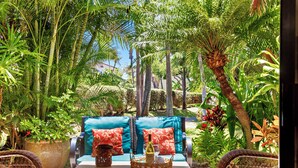 An outdoor seating area with a sofa and chairs, surrounded by lush greenery and palm trees.