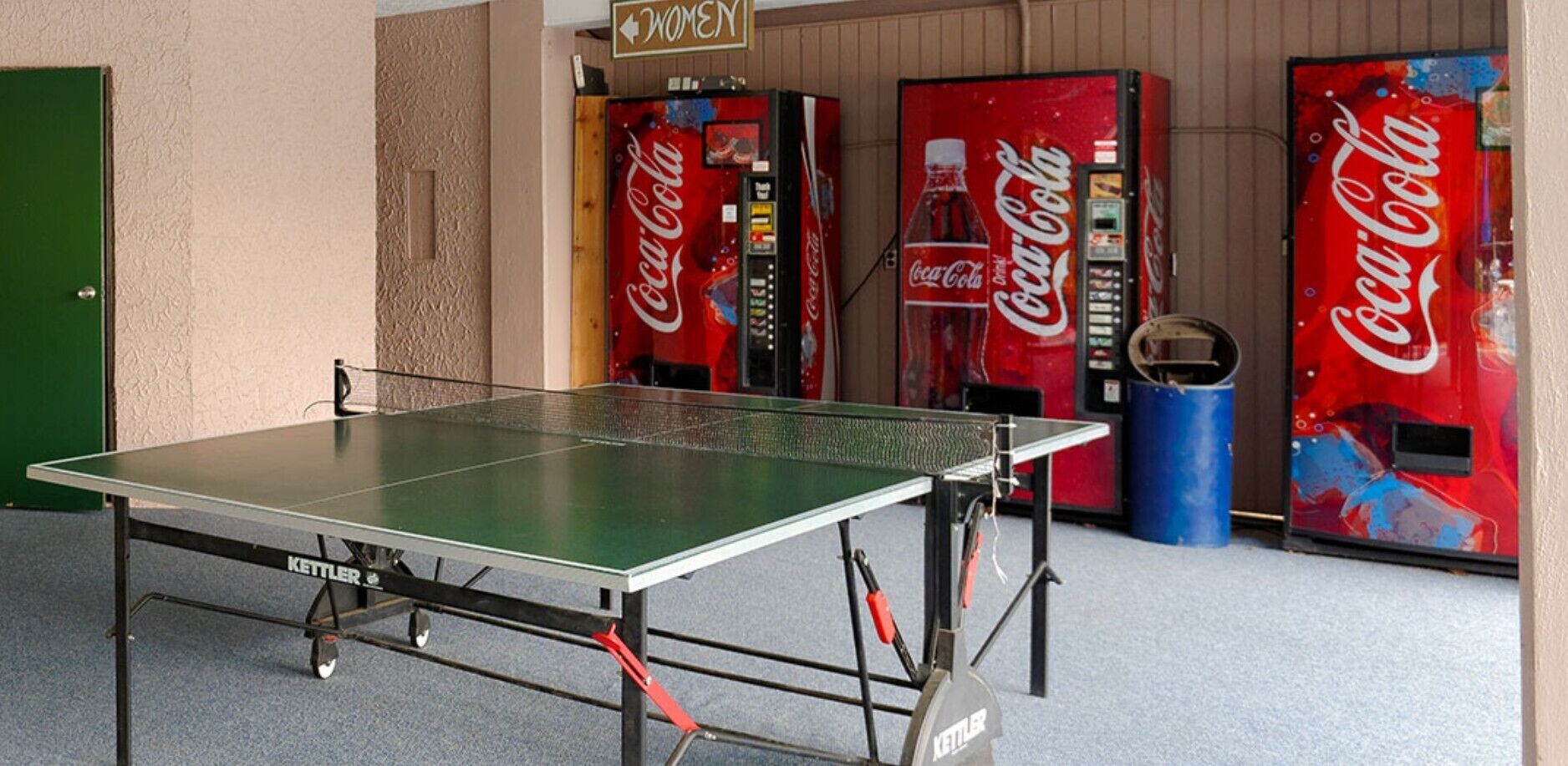 A ping pong table in front of Coca-Cola vending machines.