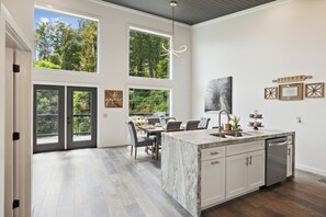 Une cuisine moderne dotée d’un grand îlot central, d’appareils électroménagers intégrés et d’un coin repas offrant une vue sur l’extérieur.