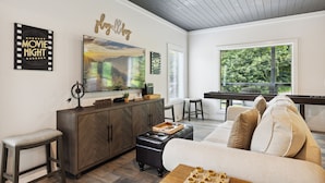 A modern living room with a herringbone-patterned cabinet, a large flat-screen TV, a wooden coffee table, and a beige sofa. - New Modern Cabin:  Fire Pit, Hot Tub, WiFi, High-End Decor and Amazing Game Room (Gatlinburg)