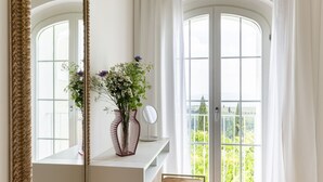 Una habitación con un espejo grande, un florero con flores, un banco y vistas a través de un ventanal.