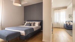 A modern bedroom with a large bed, a bedside table, a hanging light fixture, and a view into an adjacent living area. - Santa Croce Design Apartment R&R (Venecia)