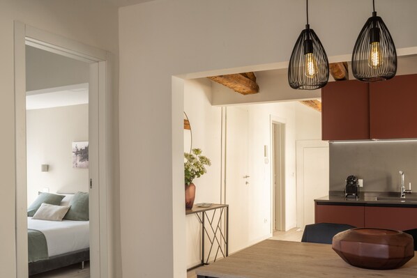 A modern kitchen with a built-in oven, a dining table with a brown bowl, and a small side table with a plant.
