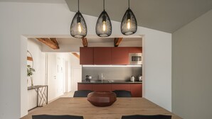 A modern kitchen with red cabinets, a wooden dining table, and black chairs. There are three pendant lights hanging above the table. - Sant'Aponal Cozy Apartment with Terrace R&R (Venecia)