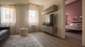 A modern living room with a flat-screen TV, a sofa, and a small ottoman. - Sant'Aponal Cozy Apartment with Terrace R&R (Venecia)