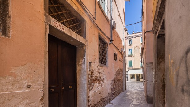 A narrow alleyway with a dark wooden door and a building with a visible address sign. - Sant'Aponal Cozy Apartment with Terrace R&R (Venecia)