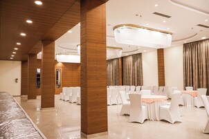 A banquet hall with white chairs, round tables, and a chandelier.