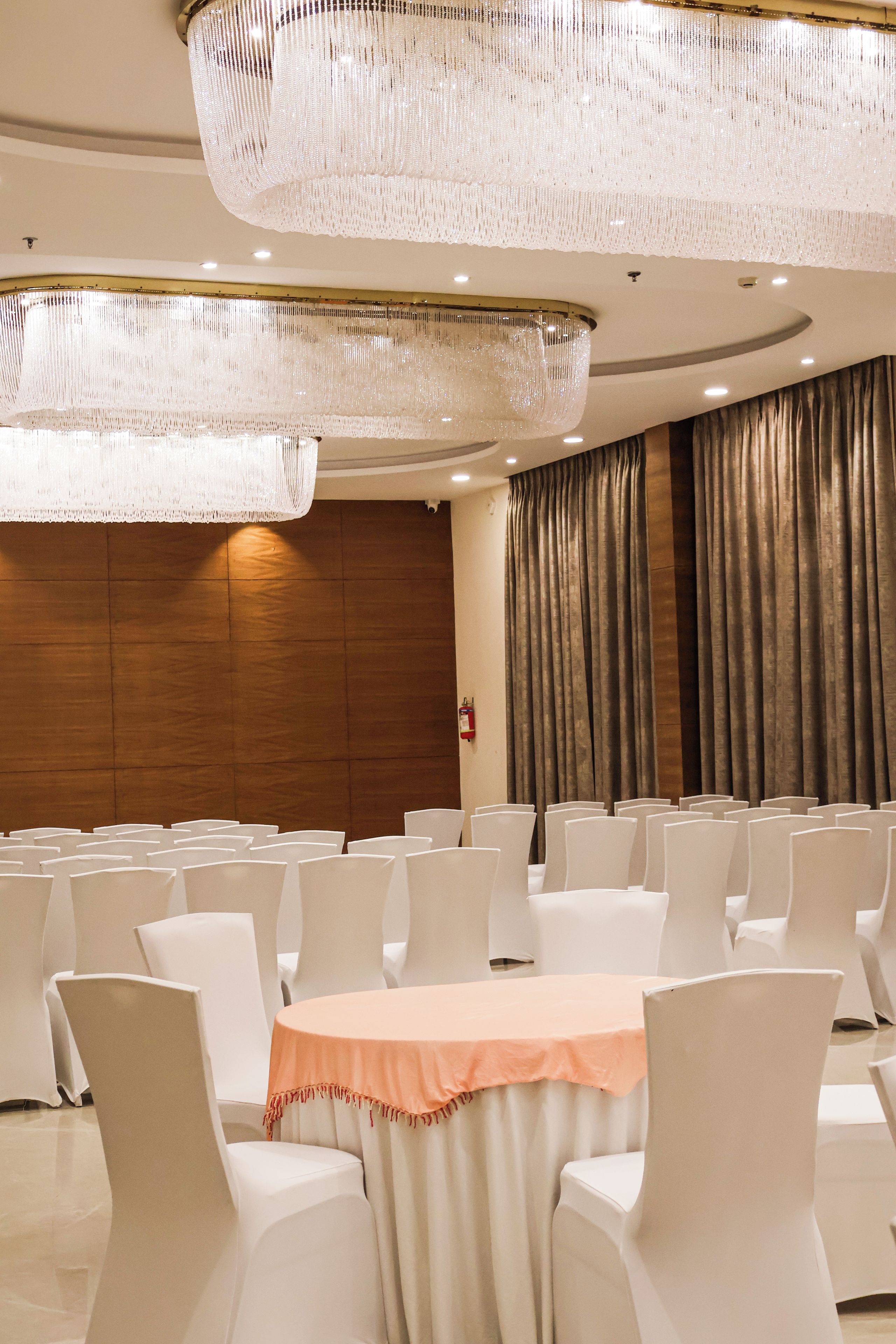 A conference room with rows of chairs, a central table with a tablecloth, and a large chandelier.