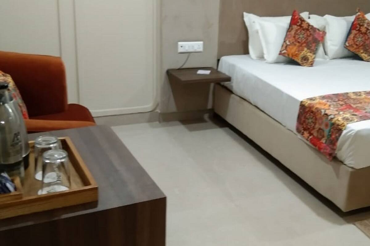 A hotel room with a bed, a nightstand, a coffee maker, a tray with cups, and an orange chair.