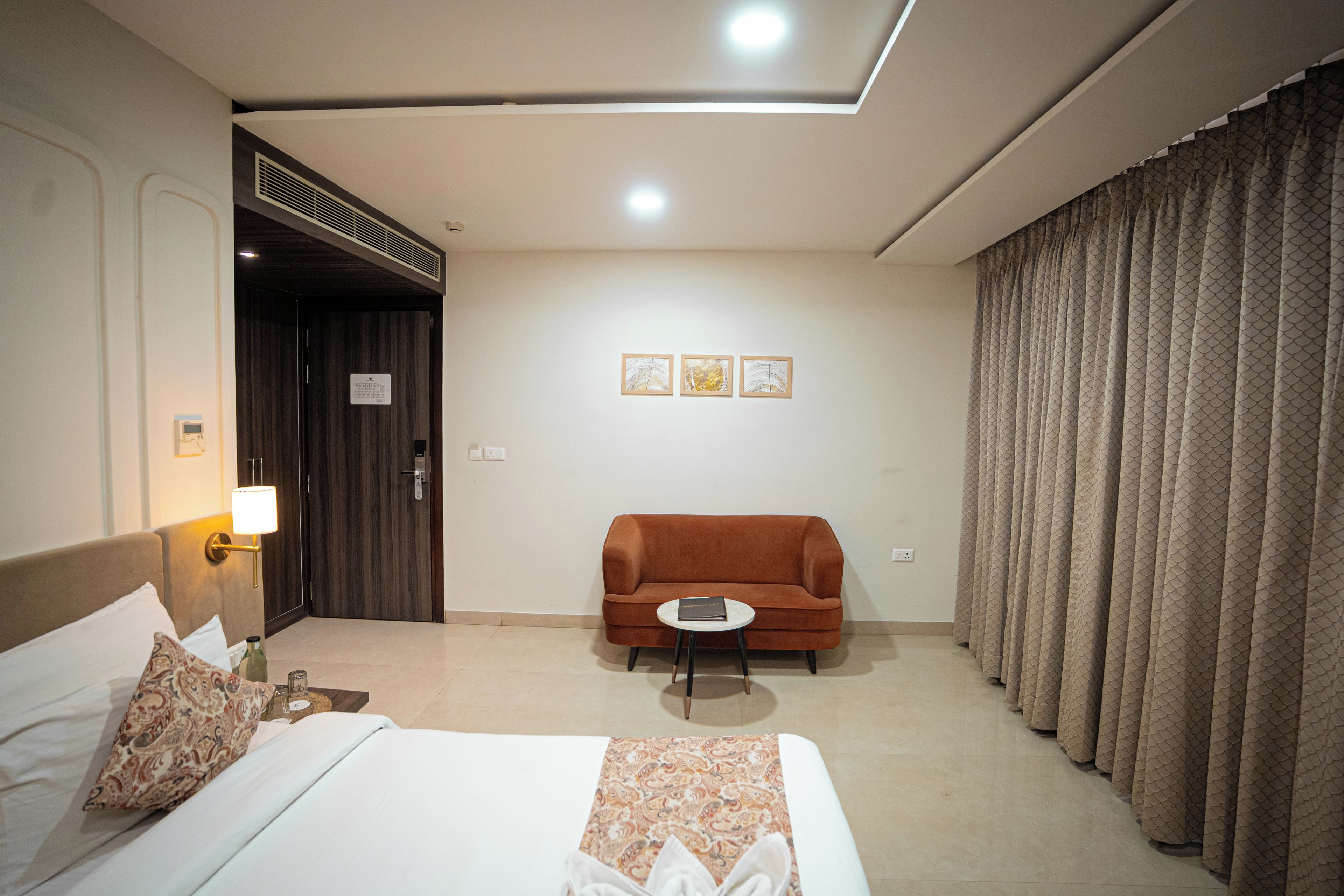 Una habitación de hotel con cama, sofá, una mesita y ventana con cortinas.