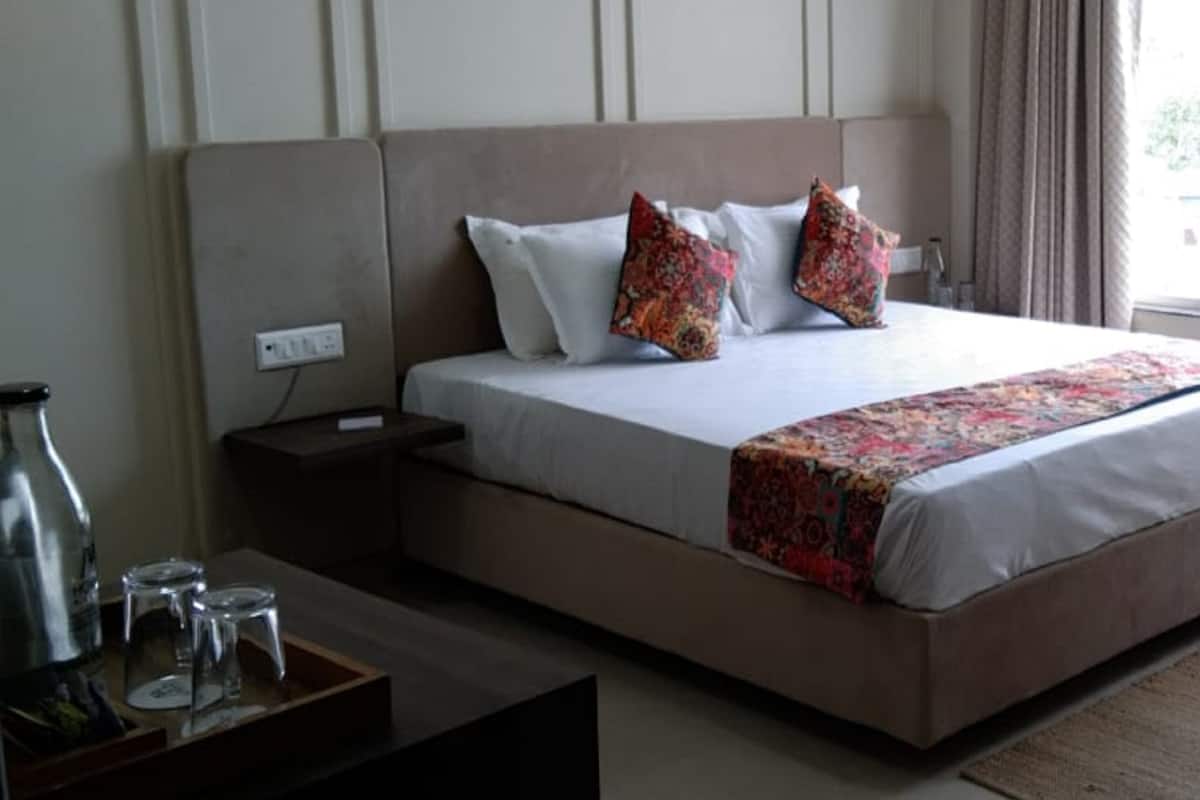 A neatly made bed with a floral bedspread, a bedside table with a lamp, and a window with curtains.
