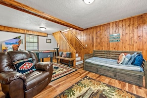 A cozy room with a brown leather couch, a wooden bed, a foosball table, and a staircase. - Walk to Dollywood*5 Min to PF* Hot Tub+Game Room (Sevierville)