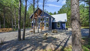 Eine Holzhütte mit Metall-Dach und großen Fenstern, umgeben von Bäumen und Kies.