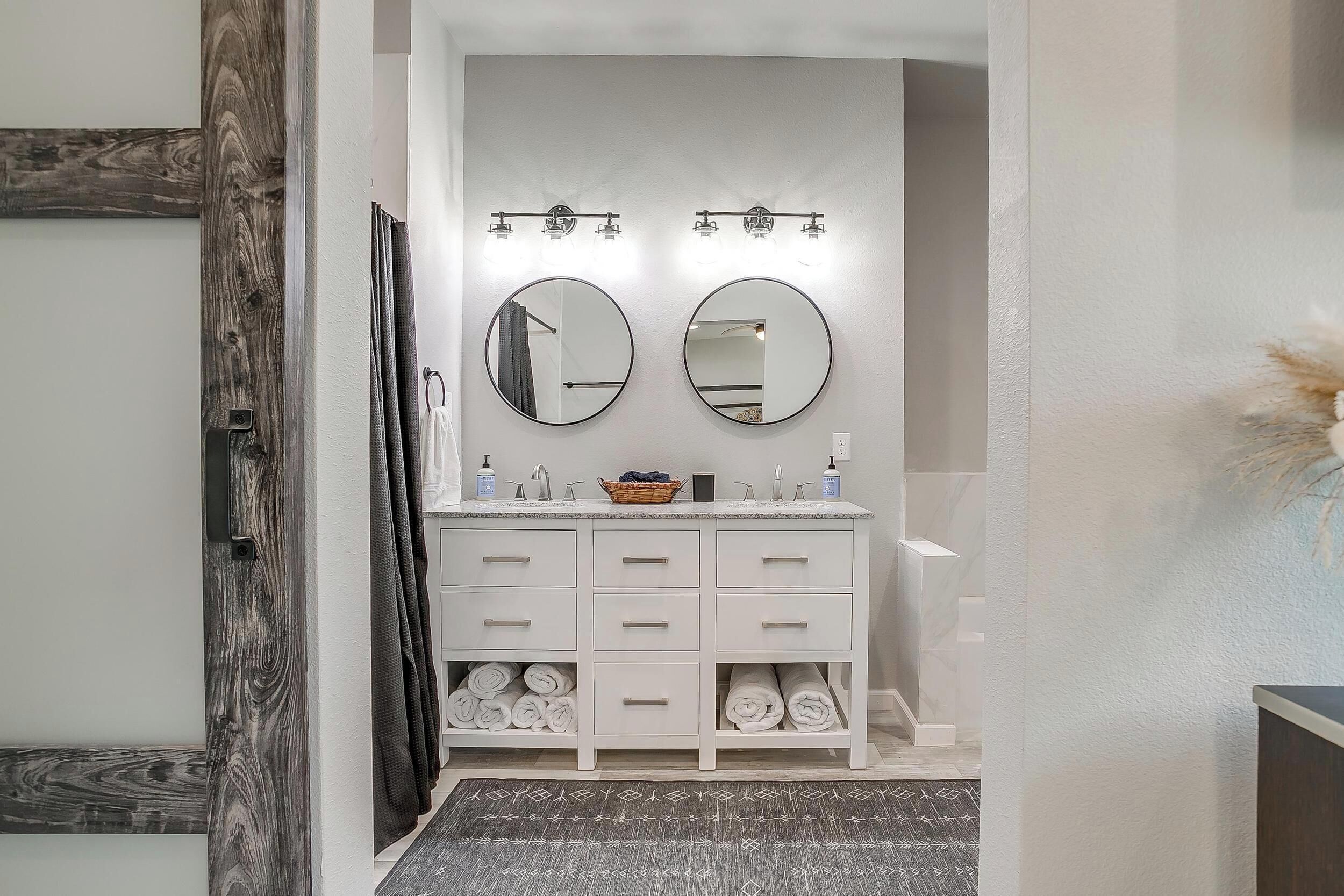 Une salle de bain avec un meuble-lavabo blanc, deux miroirs, un porte-serviettes et un rideau de douche.