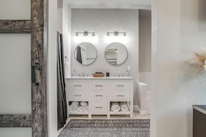 Une salle de bain avec un meuble-lavabo blanc, deux miroirs, un porte-serviettes et un rideau de douche.