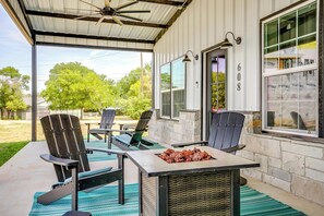 Une terrasse extérieure avec des fauteuils Adirondack, un barbecue et un espace abrité doté d’un ventilateur de plafond.
