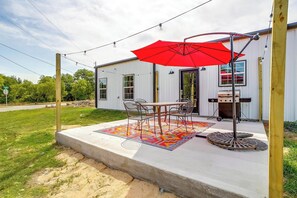 Une terrasse extérieure avec une table et des chaises, un parasol rouge et un barbecue.
