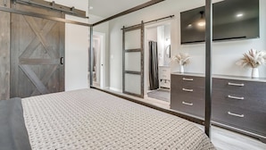 A bedroom with a large bed, a wardrobe with a mirror, a dresser, and a TV mounted on the wall.