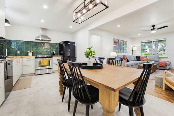 A modern kitchen with a dining area, featuring a wooden table, black chairs, and a green tiled backsplash.