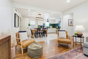 A spacious living area with a dining table, two leather chairs, a sofa, a rug, and a lamp.