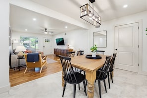 A spacious dining area with a wooden table and black chairs, a television in the background, and a ceiling fan.